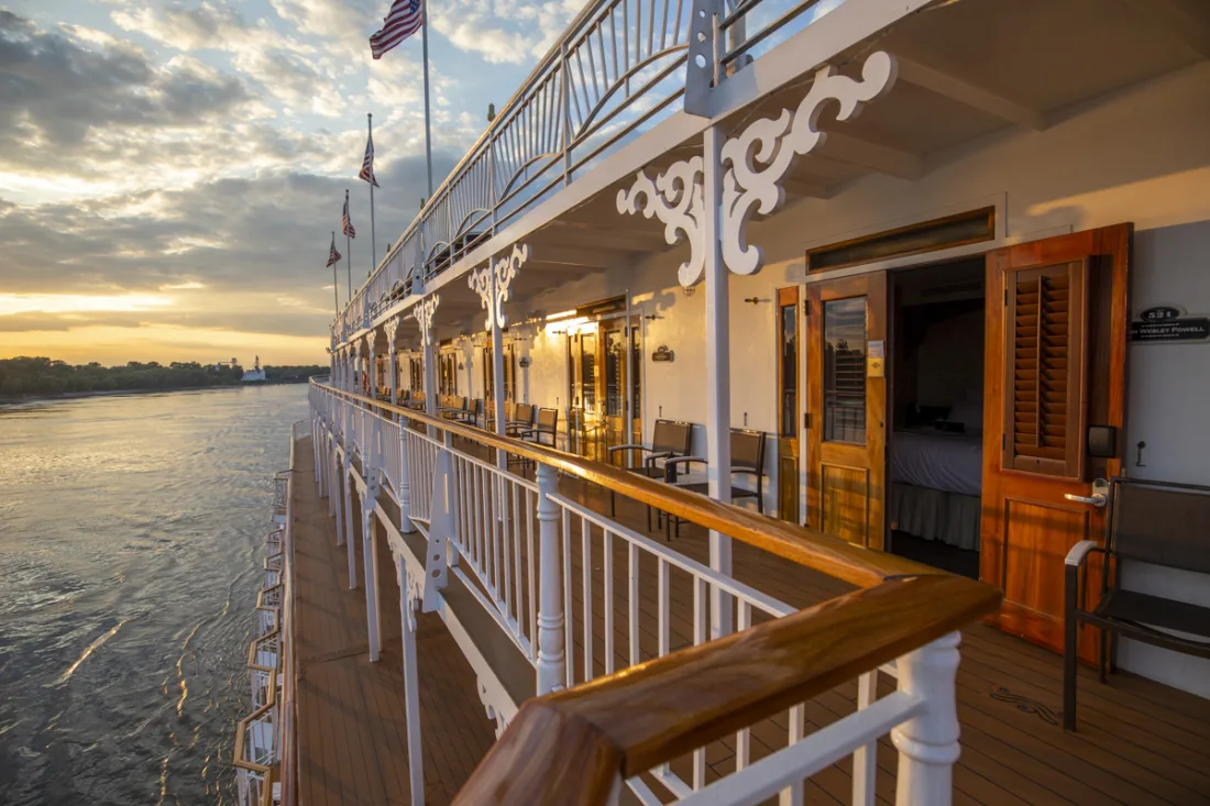 Sunset over the Mississippi from the American Queen's promenade deck, cabin doors open onto white gingerbread railings