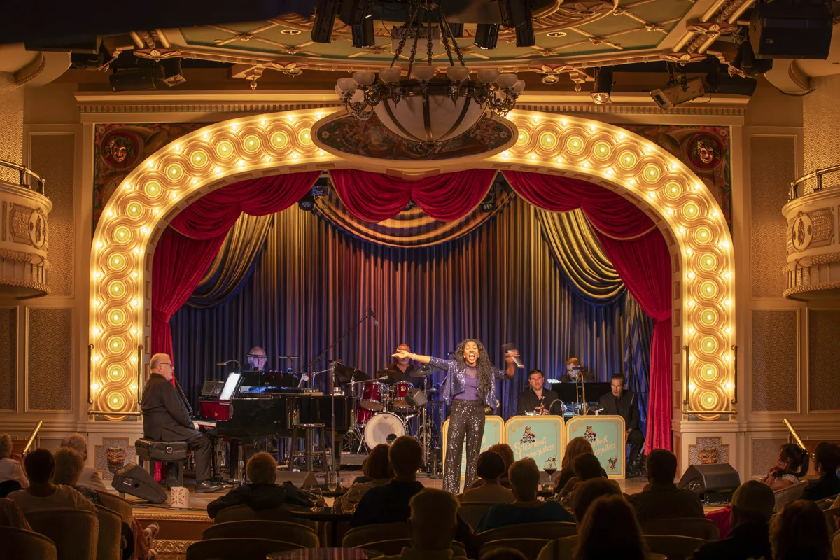 A singer in sequins performs with a live band in the American Queen's gilded theatre