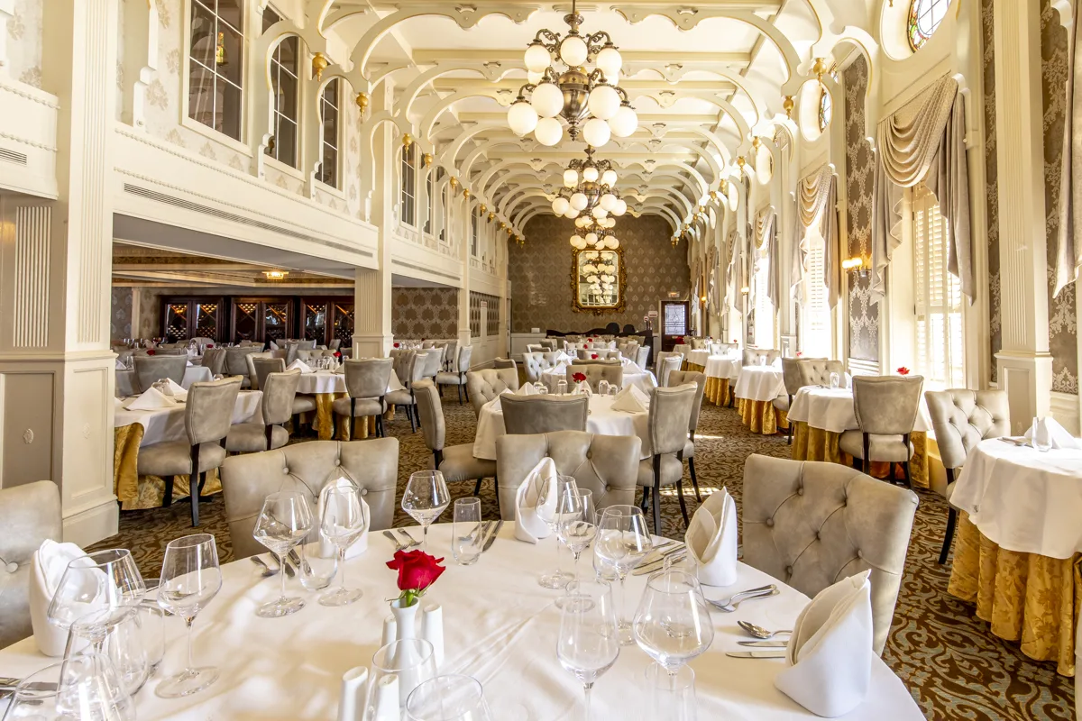 White-clothed tables set with crystal and a single red rose under the vaulted ceiling of the dining room