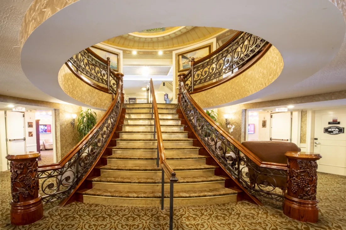 Twin curved staircases sweep up beneath an oval opening, carved newel posts and ironwork balustrades