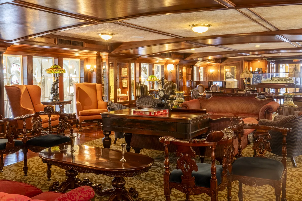 Antique chairs, chesterfields and stained glass lamps in a wood panelled lounge aboard the American Queen