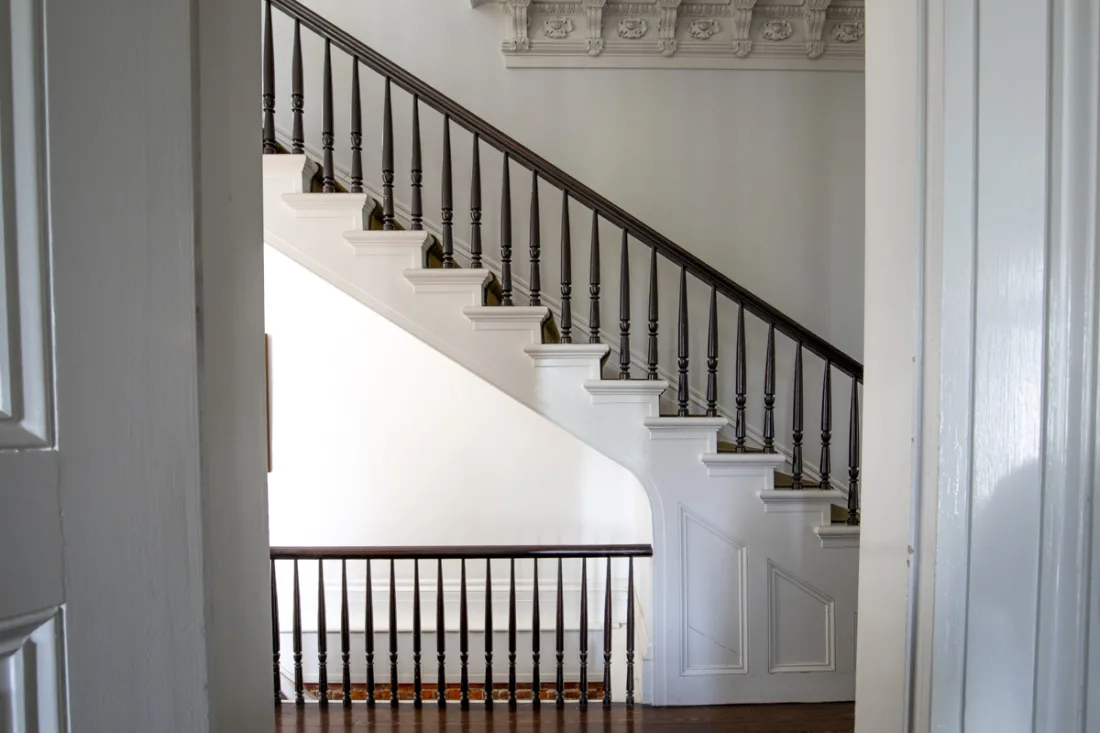 A dark timber banister curves up the white staircase of a Louisiana antebellum mansion